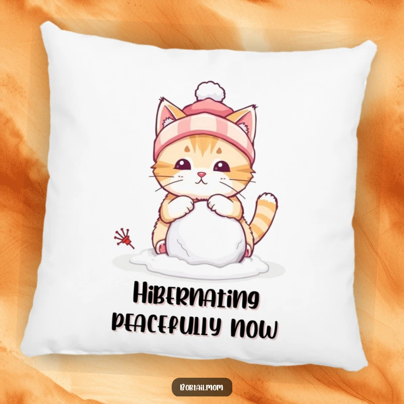 Funny pillow showcasing a bobtail cat with a winter hat, building a tiny snowball, adding a touch of winter fun.