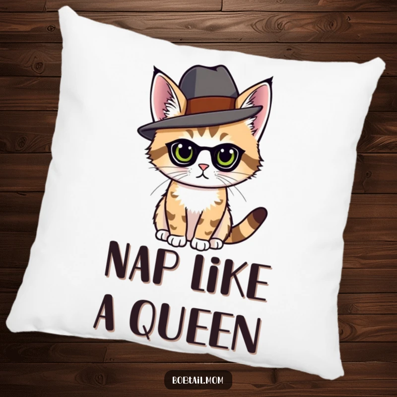 Funny bobtail cat with an elegant hat, posing with grace, on a soft, decorative pillow.