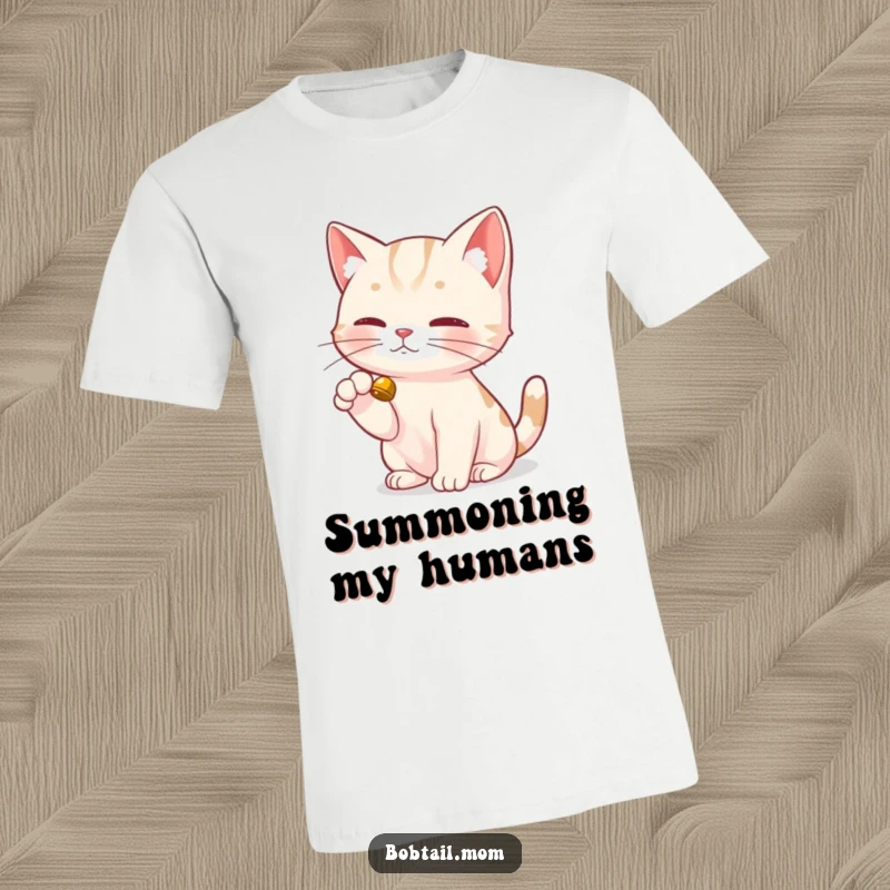 Funny Bobtail Cat T-Shirt depicting a Bobtail cat delicately tapping a small bell with its dainty paw, signaling playful intent.